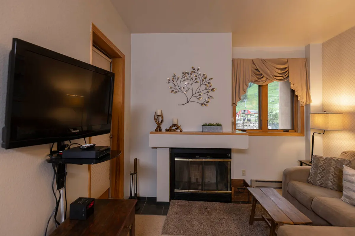 A warmly lit living room showcases a prominent fireplace with a plush sofa nearby. The window offers lovely scenic views, and the seating arrangement invites guests to relax or engage in intimate conversation. The overall mood is intimate and welcoming, perfect for cozy evenings or sharing stories by the hearth.