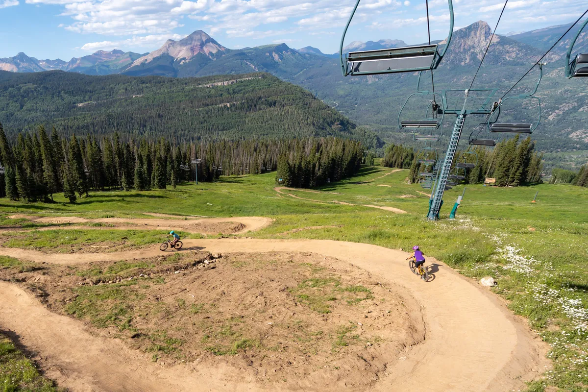 A panoramic shot of majestic mountains, ski lifts, and winding bike trails captures the all-season excitement just steps from the property. The scene invites thoughts of mountain biking, hiking, and connecting with nature.