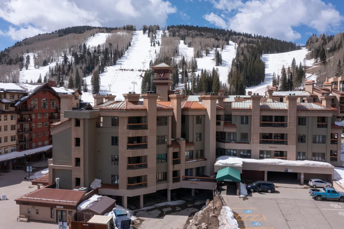 This image showcases the exterior of the building set against a breathtaking mountain backdrop. Snow-covered ski slopes and the surrounding peaks emphasize the property's proximity to winter sports and natural beauty. The scene also includes balconies for après-adventure relaxation.