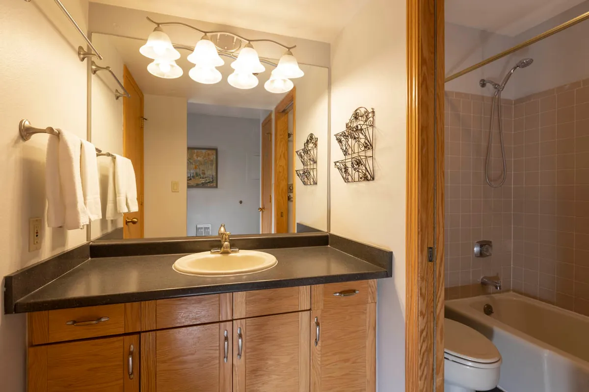 This interior image features a serene bathroom scene with a well-lit vanity mirror, modern sink, towel rack, and a spacious bathtub. The ambiance is calm and refreshing, inviting guests to unwind and indulge in self-care routines.