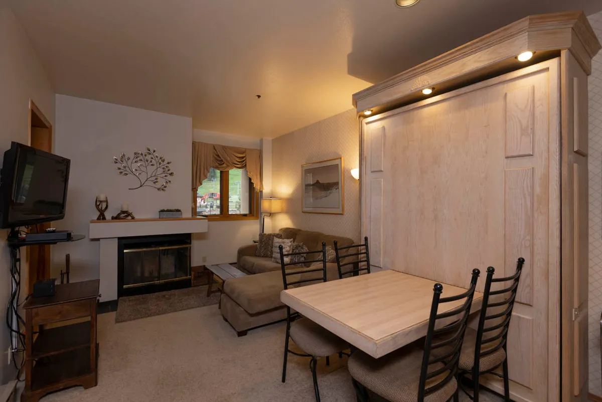 This inviting space features a fireplace, plush sofa, and a dining table, all bathed in natural light from a large window. The arrangement suits family gatherings, board games, or casual dining, and the vibe is both cozy and versatile.
